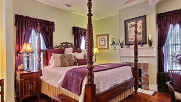 A four-poster bed with a wooden headboard, a nightstand with a lamp, and a chair with a cushion.