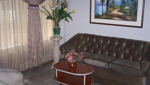 A living room with a brown leather sofa, a small wooden coffee table with a vase of flowers, and a framed landscape painting on the wall. - Imperium Hotel Lima (Lima)