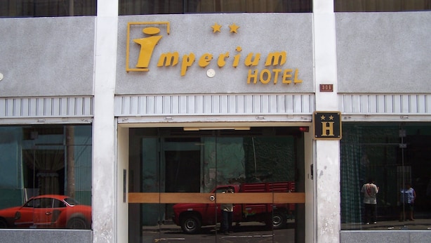The exterior of the Imperium Hotel with a large glass entrance, a red vehicle parked inside, and a visible person standing near the entrance. - Imperium Hotel Lima (Lima)