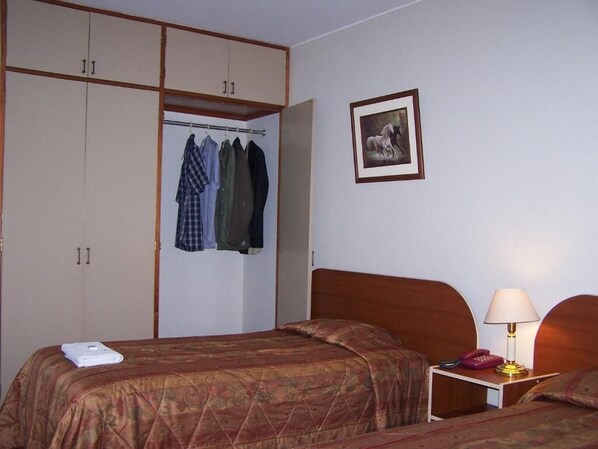 A hotel room with two beds, a wardrobe, a framed picture on the wall, and a bedside table with a lamp. - Imperium Hotel Lima (Lima)