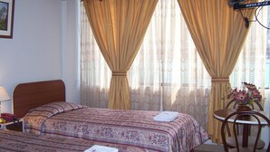 A hotel room with a bed, a bedside table with a lamp, a chair, and a small table with a vase of flowers. - Imperium Hotel Lima (Lima)