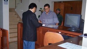 A reception area with a wooden desk, a computer monitor, and a staircase in the background. - Imperium Hotel Lima (Lima)