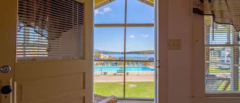 A view from a room with a door leading to a balcony overlooking a pool area.