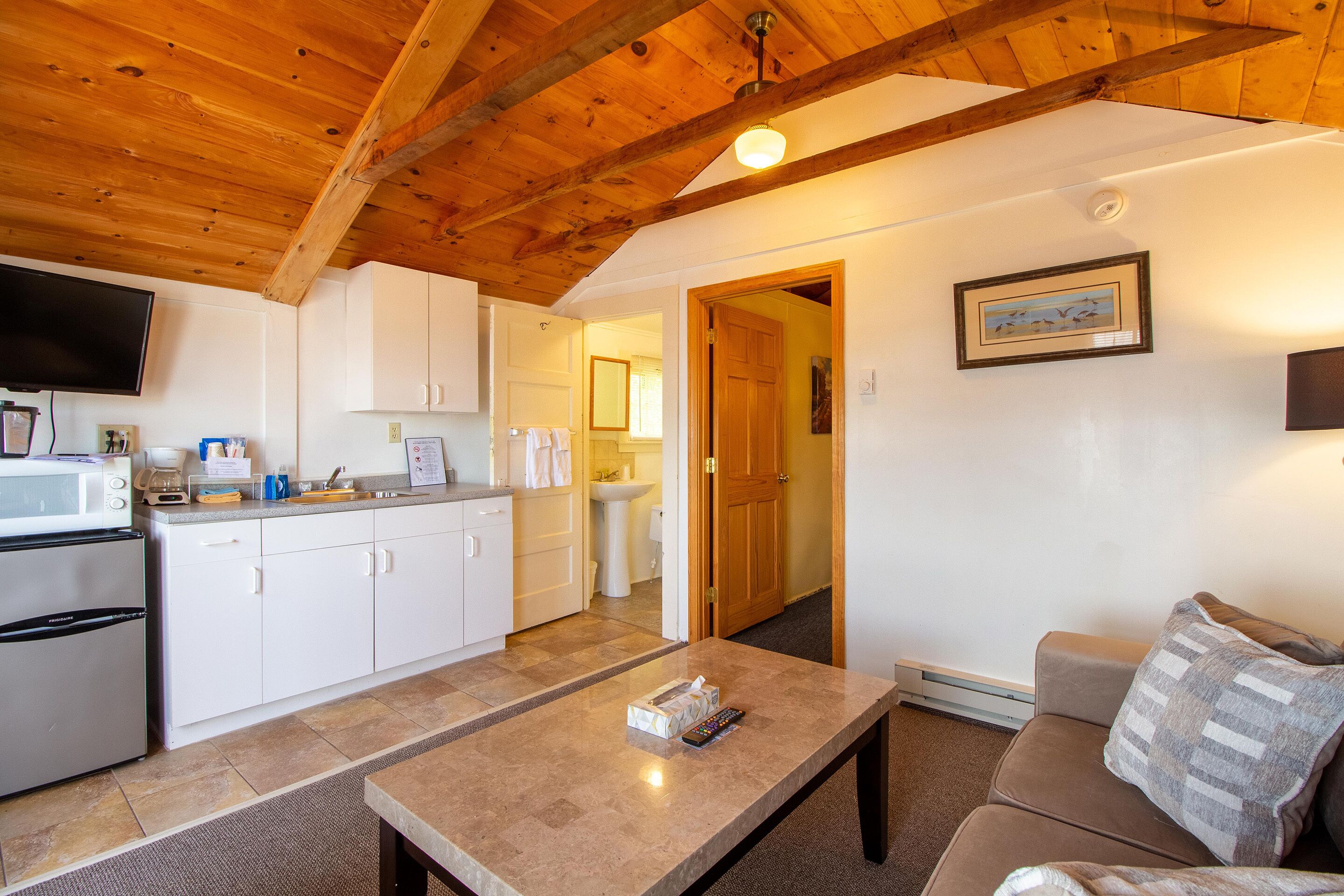 A kitchen with white cabinets, a microwave, and a refrigerator. There is a dining table with a remote control on it.