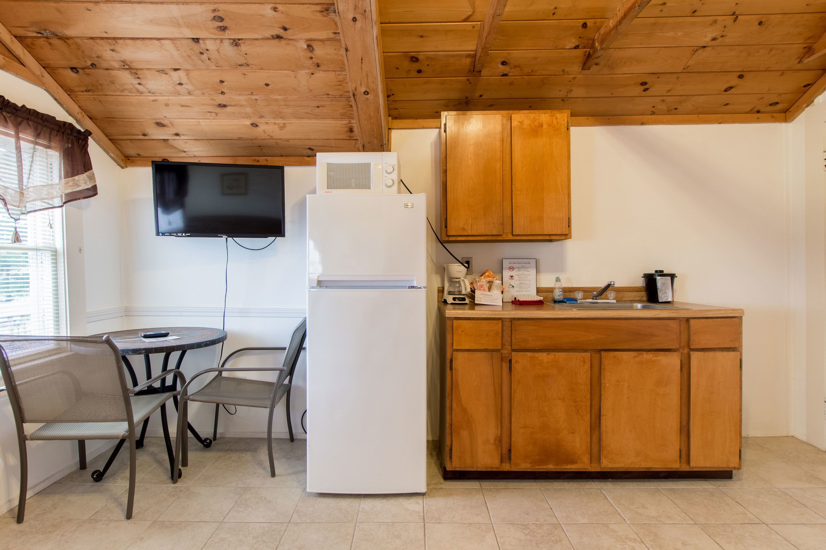 A compact kitchen with a refrigerator, microwave, wooden cabinets, a sink, and a dining area with chairs and a table.