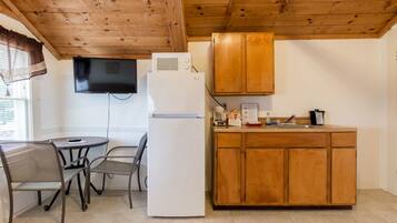 A compact kitchen with a refrigerator, microwave, wooden cabinets, a sink, and a dining area with chairs and a table.