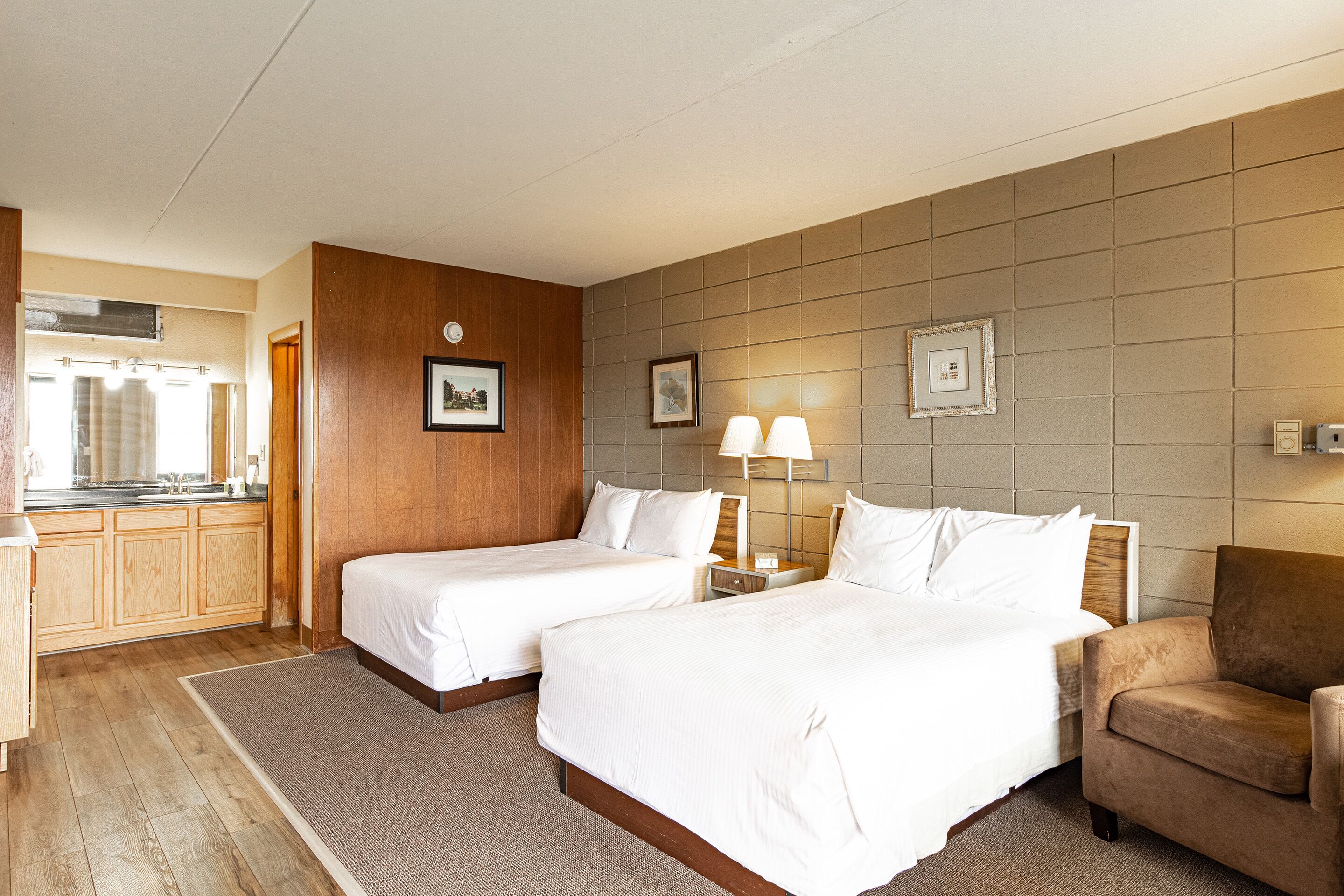 A hotel room with two beds, a sofa, a small table, and a kitchenette.