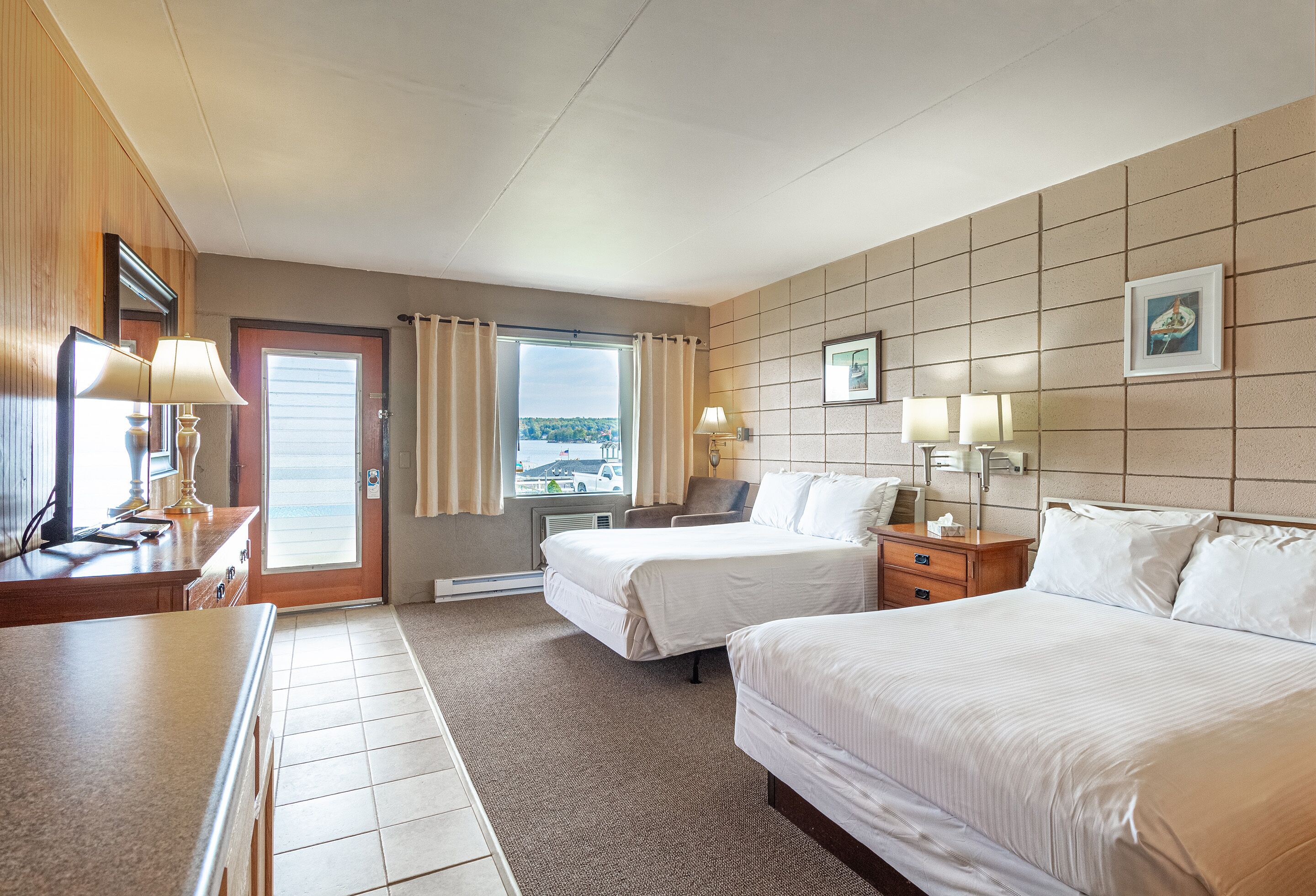 A hotel room with two beds, a desk, a chair, a window with curtains, and a view of the outside.