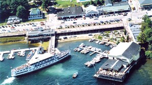 Vista aérea de una zona costera con un gran crucero amarrado, un puerto deportivo con varias embarcaciones y una hilera de casas a lo largo de la orilla.