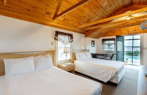 Quarto de hotel com duas camas, vigas de madeira no teto, uma mesa e vista para uma piscina.