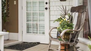 Een veranda met een witte deur, een schommelstoel en een bloempot.