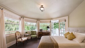 Een slaapkamer met een groot bed, een stoel, een bureau en uitzicht op het groen door grote ramen.