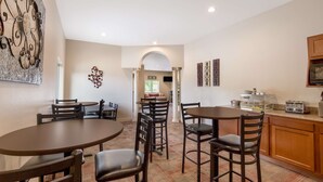 A dining area with round tables and chairs, a kitchen with a countertop and appliances, and a hallway leading to another room.
