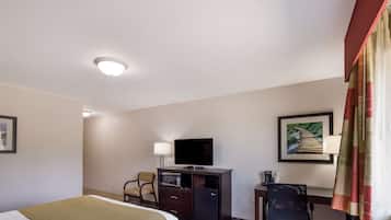 Een hotelkamer met een bed, een bureau met een computer, een televisie, een kleine koelkast en een stoel.