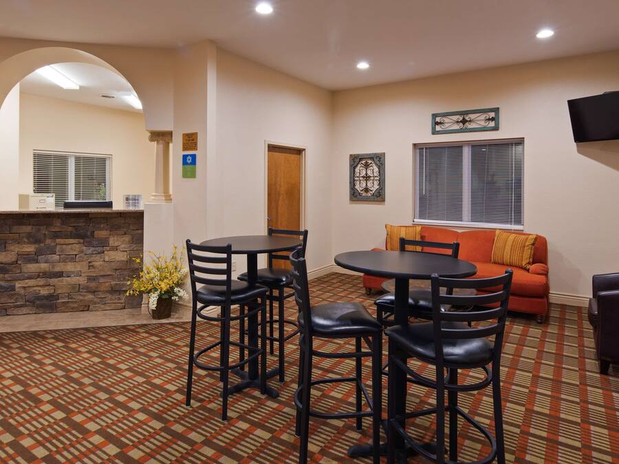 A hotel lobby with a stone fireplace, a round table with chairs, a sofa, and a television mounted on the wall.