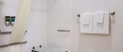 A bathroom with a shower, a towel rack with two towels, and a small shelf with toiletries.