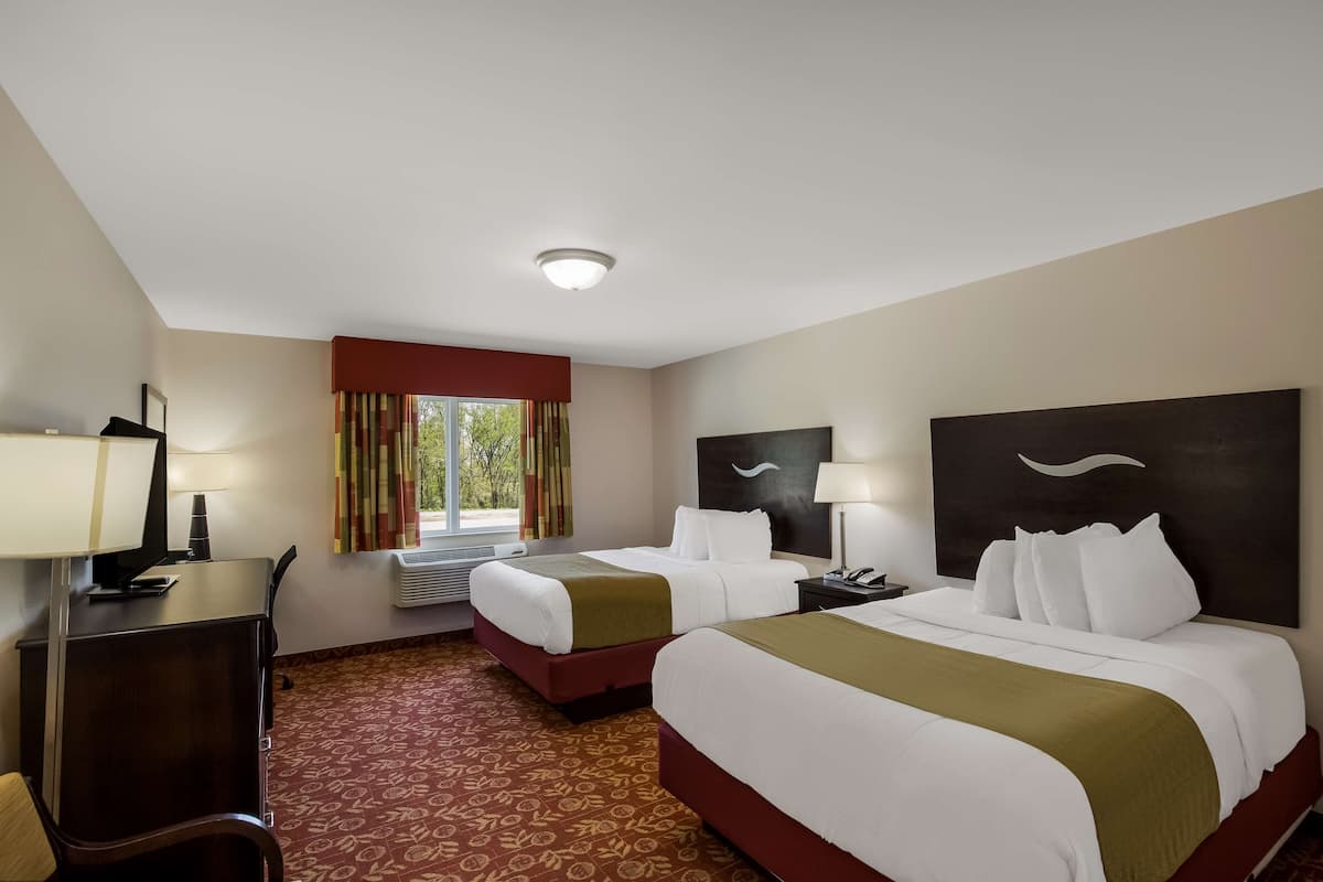 A hotel room with two beds, a desk, a chair, a TV, and a window with curtains.