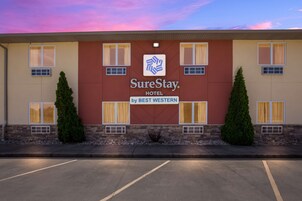 Um hotel SureStay by Best Western com fachada em vermelho e bege, várias janelas e duas árvores verdes em vasos na frente.