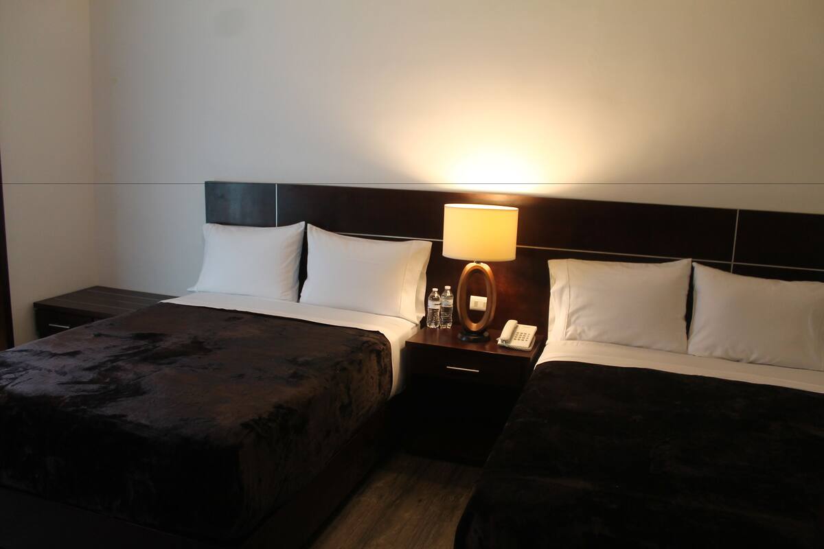 A hotel room with two beds, a nightstand with a lamp, and a phone.