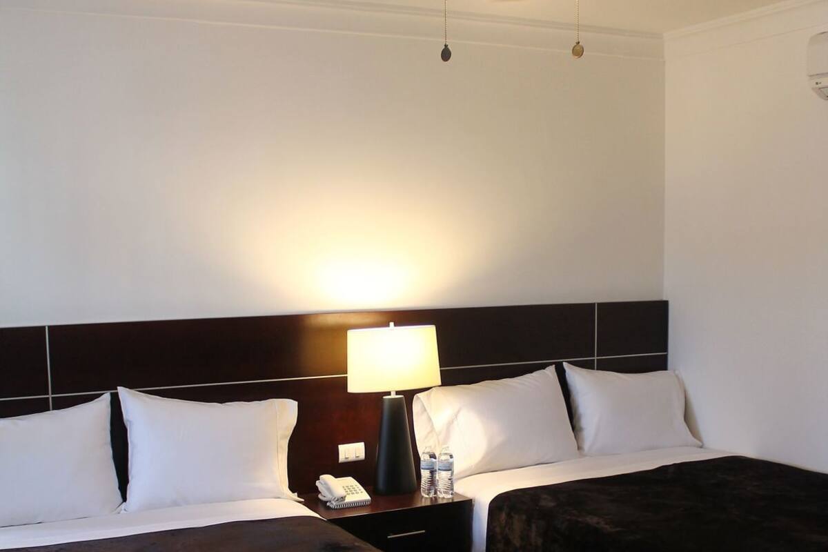 A hotel room with two beds, a ceiling fan, a bedside lamp, a nightstand, and a water bottle.