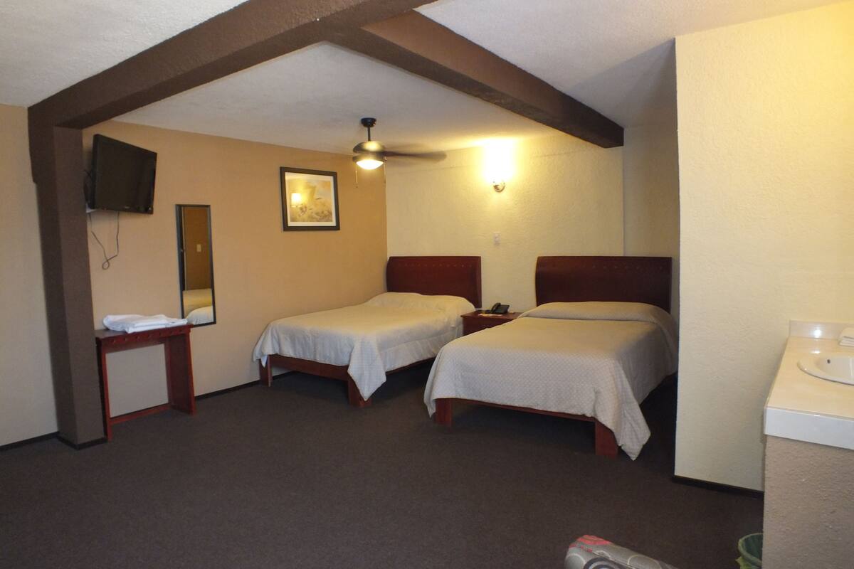 A hotel room with two single beds, a small table, a television, and a ceiling fan.