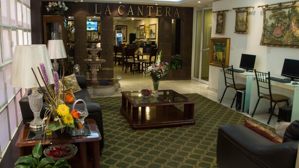 A hotel lobby with a dining area, a reception desk, and a seating area with a coffee table and lamps. - Hotel Rincón Real Suites (Durango)