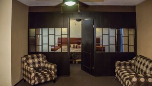 A hotel room with a bed, two armchairs, a ceiling fan, and a view through a door. - Hotel Rincón Real Suites (Durango)