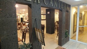 The entrance to La Cantera with a stone facade, indoor seating area, and a glass door leading inside. - Hotel Rincón Real Suites (Durango)