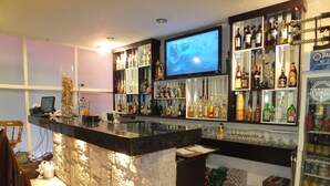 A bar area with a TV screen, shelves of liquor bottles, and a refrigerator. - Hotel Rincón Real Suites (Durango)