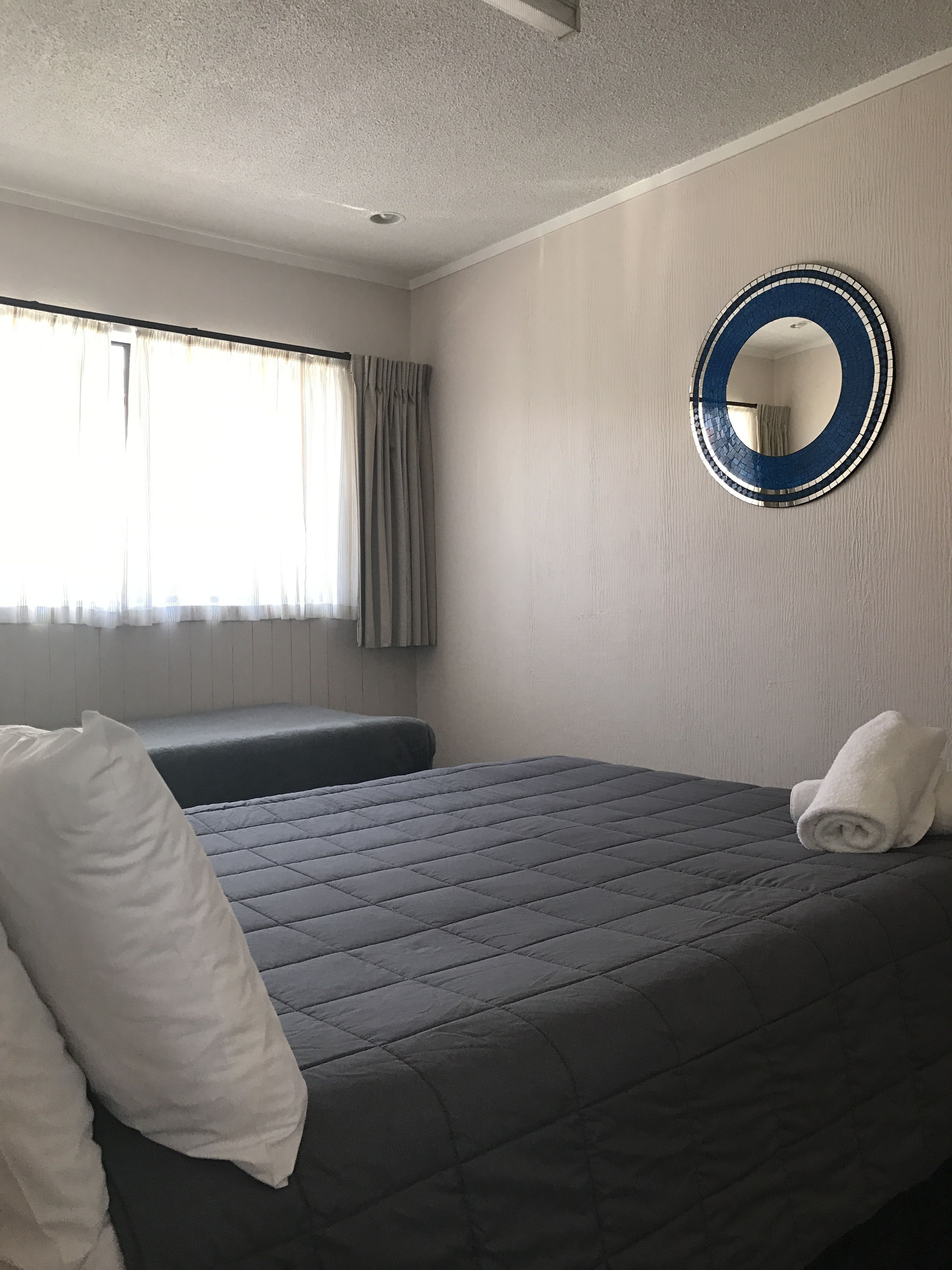 A hotel room with a bed, a round mirror, and a window with curtains.