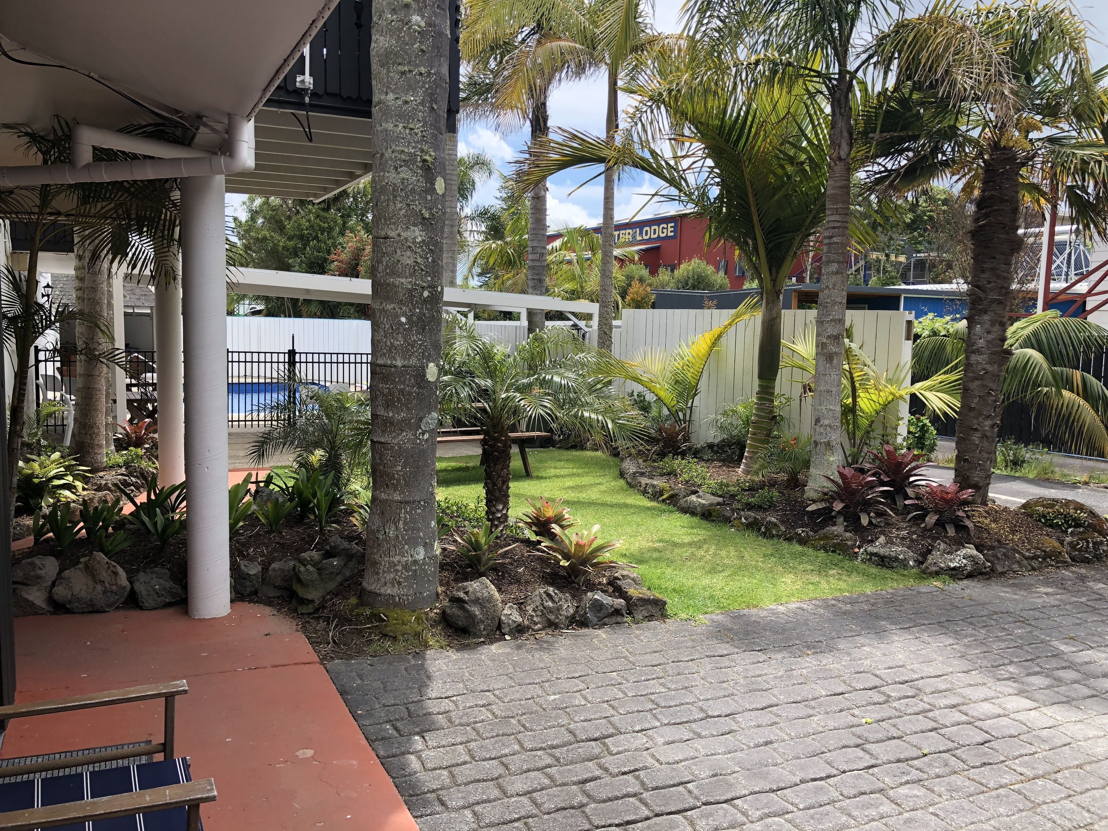 Un jardin tropical avec des palmiers, un chemin bordé de briques et un bâtiment portant l’inscription « Lodge ».