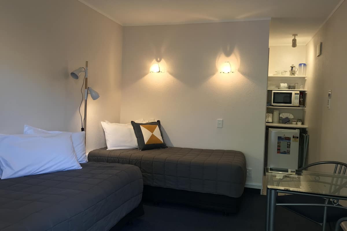 A compact hotel room with two single beds, a small kitchenette, and a glass table.