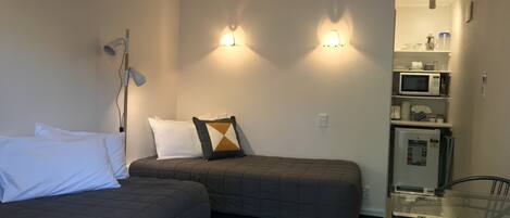 A compact hotel room with two single beds, a small kitchenette, and a glass table.