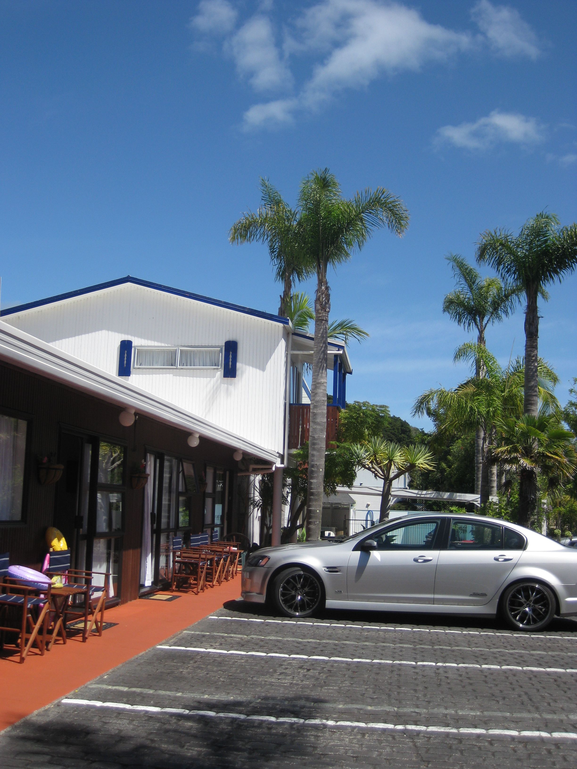 Un edificio con fachada blanca y detalles azules, un estacionamiento y varias palmeras.