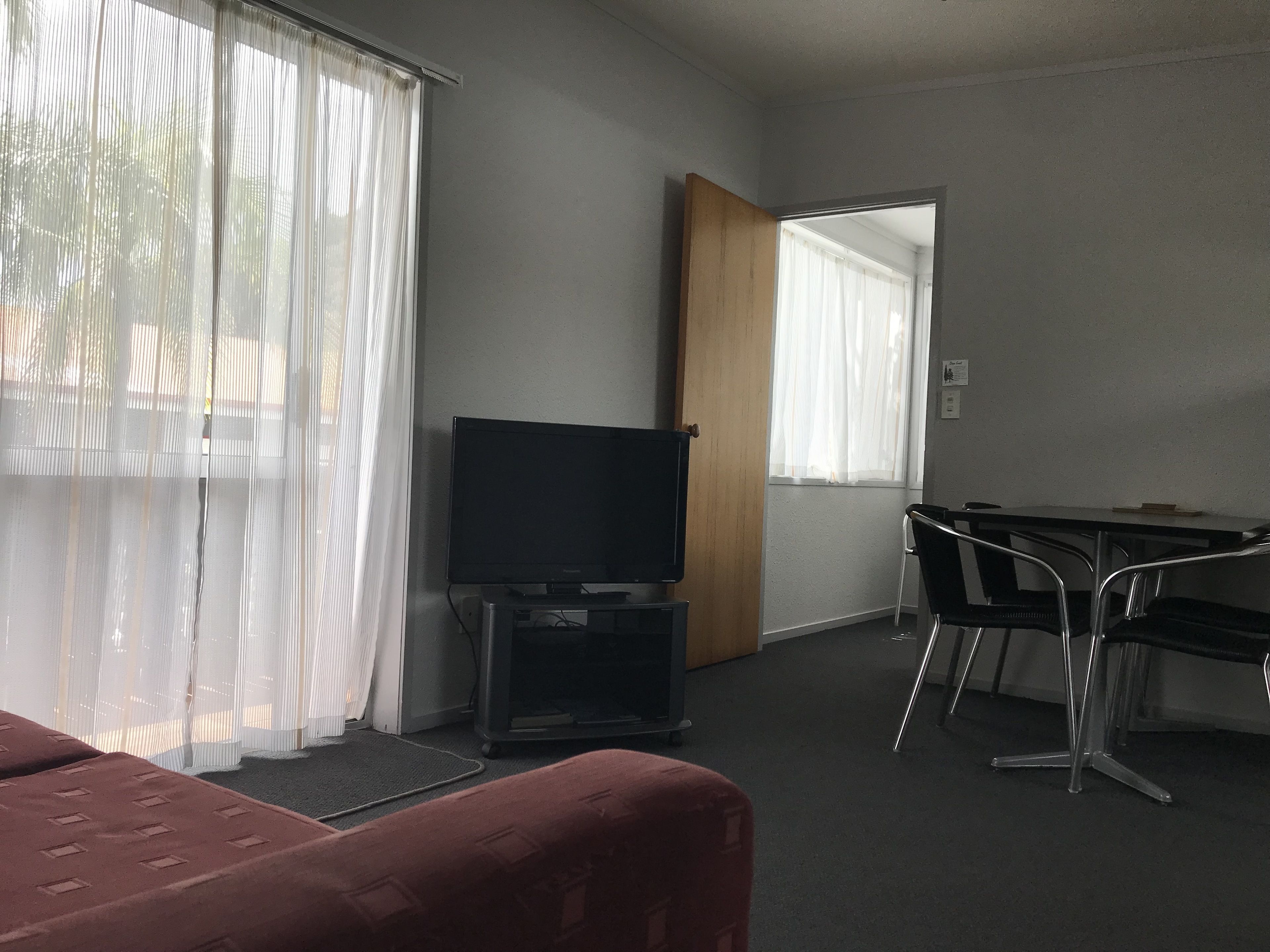Una stanza con TV su un mobile, una scrivania con sedie e una porta che conduce a un'altra stanza.