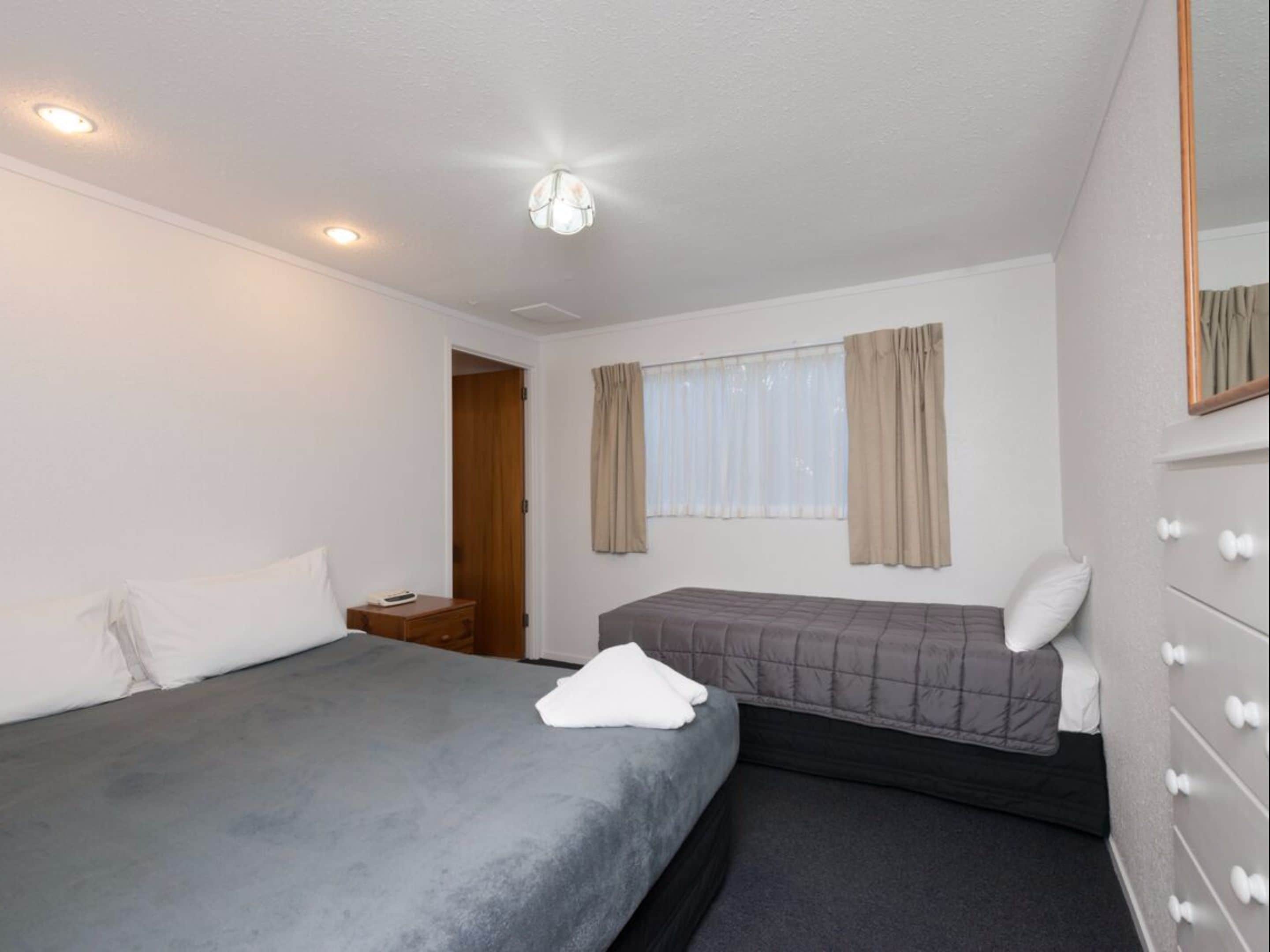 Ein Hotelzimmer mit zwei Betten, einer Holztür, einem Fenster mit Vorhängen und einem Spiegel an der Wand.