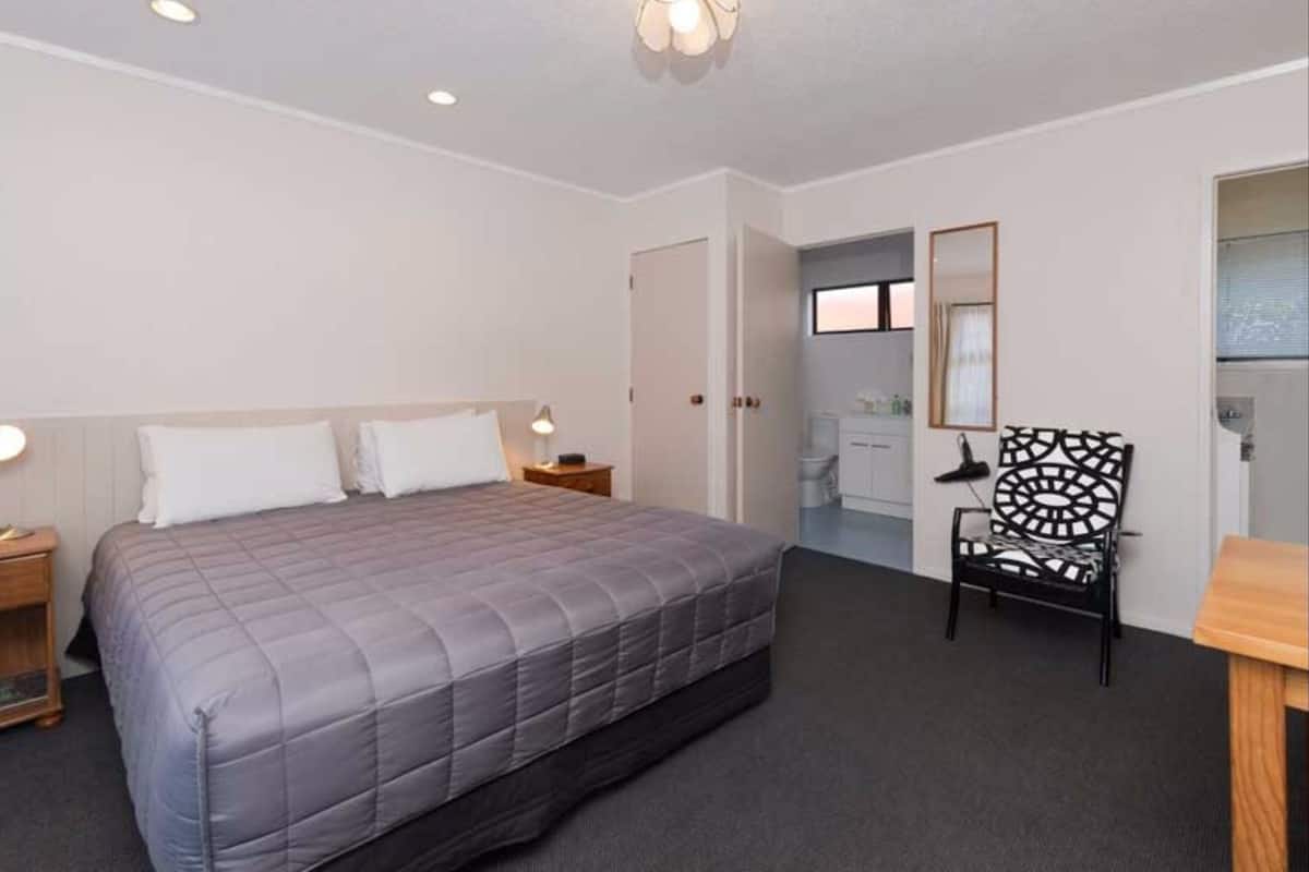 A hotel room with a bed, bedside lamps, a desk with a chair, and a bathroom visible through an open door.