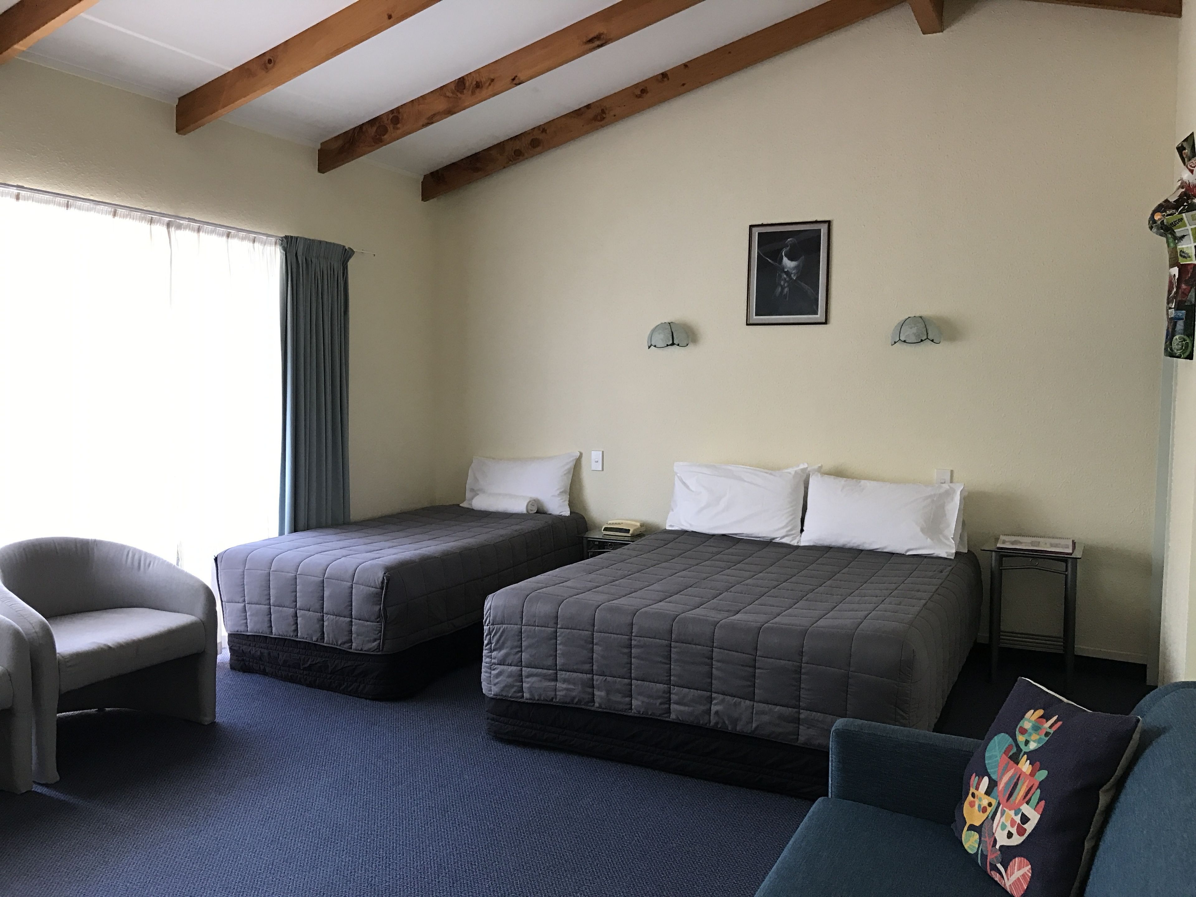 Ein Hotelzimmer mit zwei Betten, einem Sessel, einem Schreibtisch und einem Fenster mit Vorhängen.