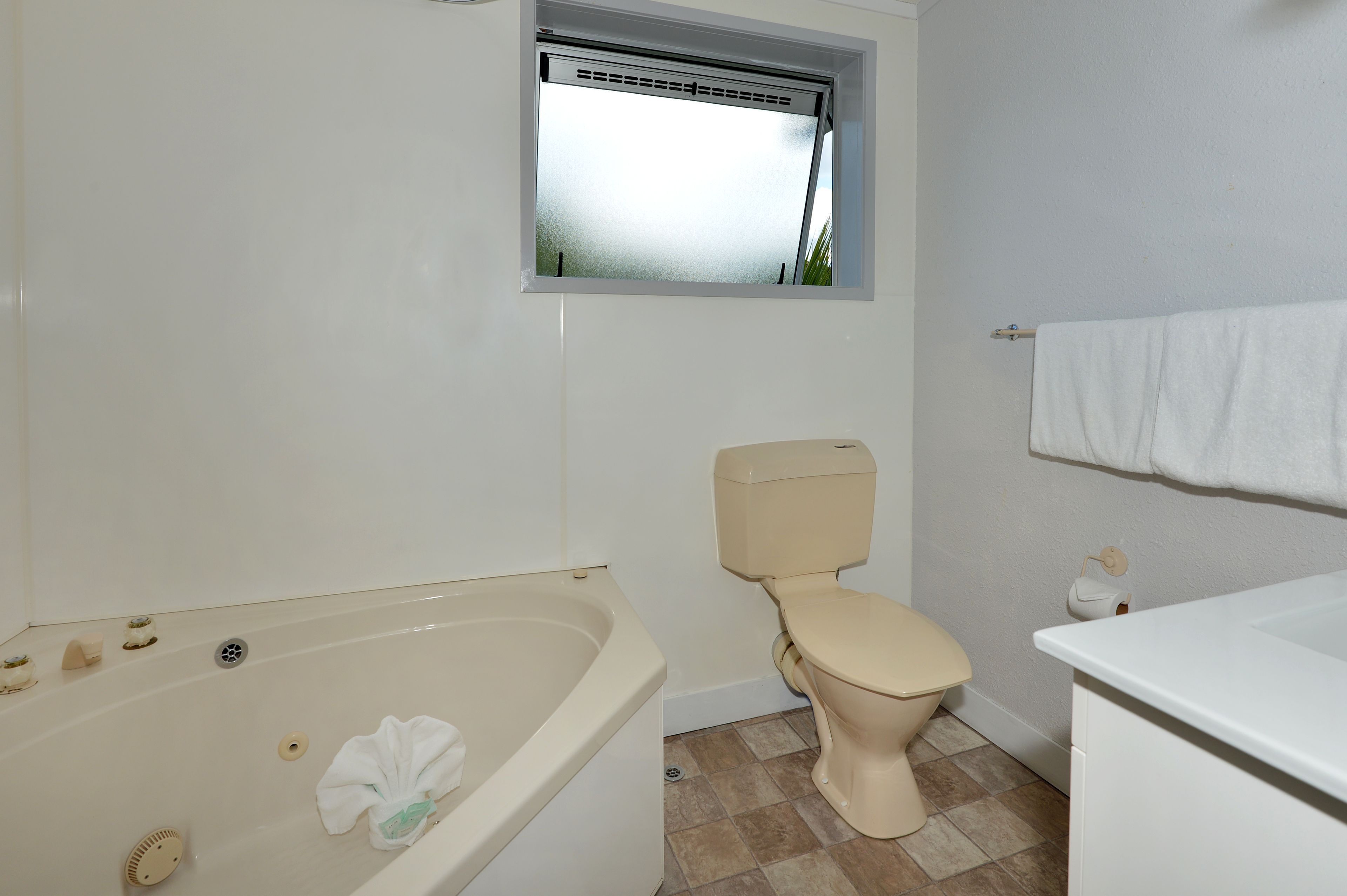 Een badkamer met een bad, toilet en een raam boven het toilet.