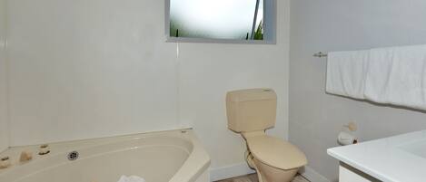 Een badkamer met een bad, toilet en een raam boven het toilet.
