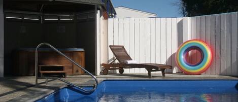 Una piscina con terraza de madera, una silla de descanso y un flotador inflable de colores.