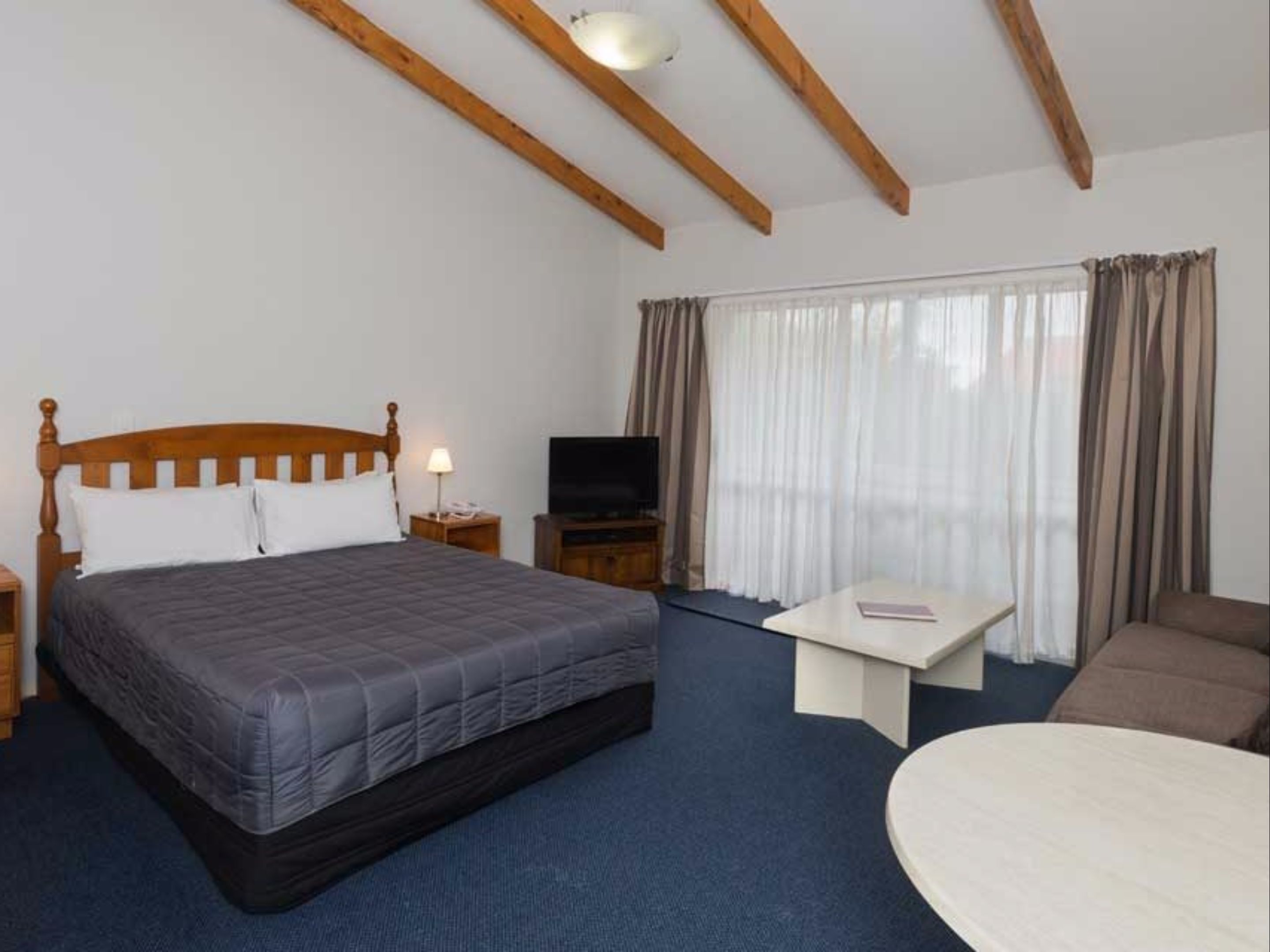 Une chambre d’hôtel avec un lit en bois, une télévision, une petite table et un canapé.