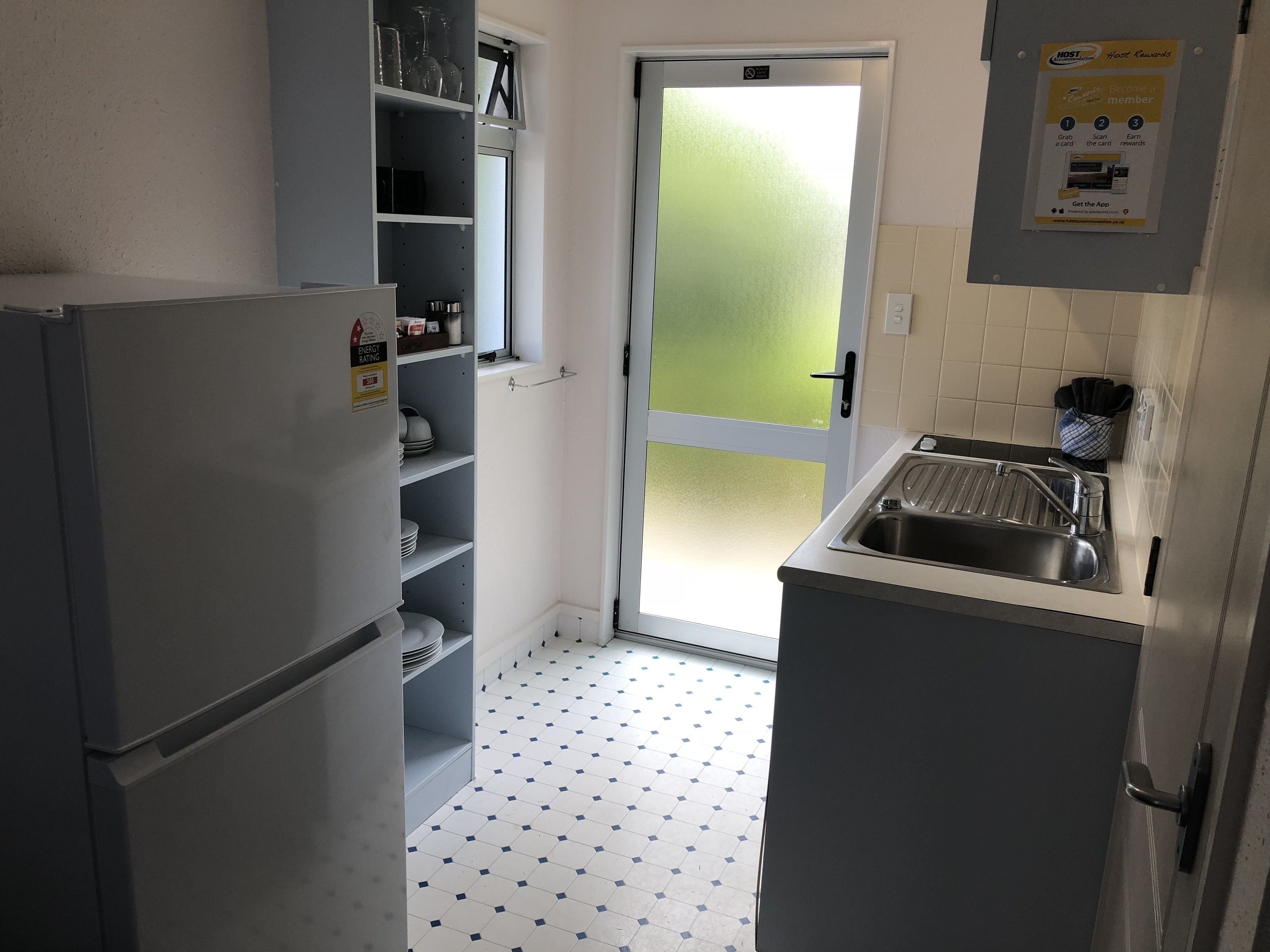 Eine kleine Küche mit Kühlschrank, Spüle und einer Tür, die auf einen Balkon führt.