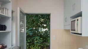 A kitchen with a glass door leading to a garden, a microwave, and shelves with jars and kitchen items. - Edelweiss Motel (Paihia)