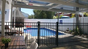A covered outdoor area with a pool, a fenced patio, and a restaurant in the background. - Edelweiss Motel (Paihia)