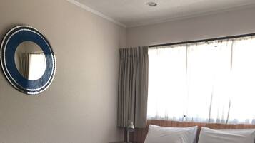 A hotel room with a large bed, a round mirror, a nightstand, and a window with curtains.