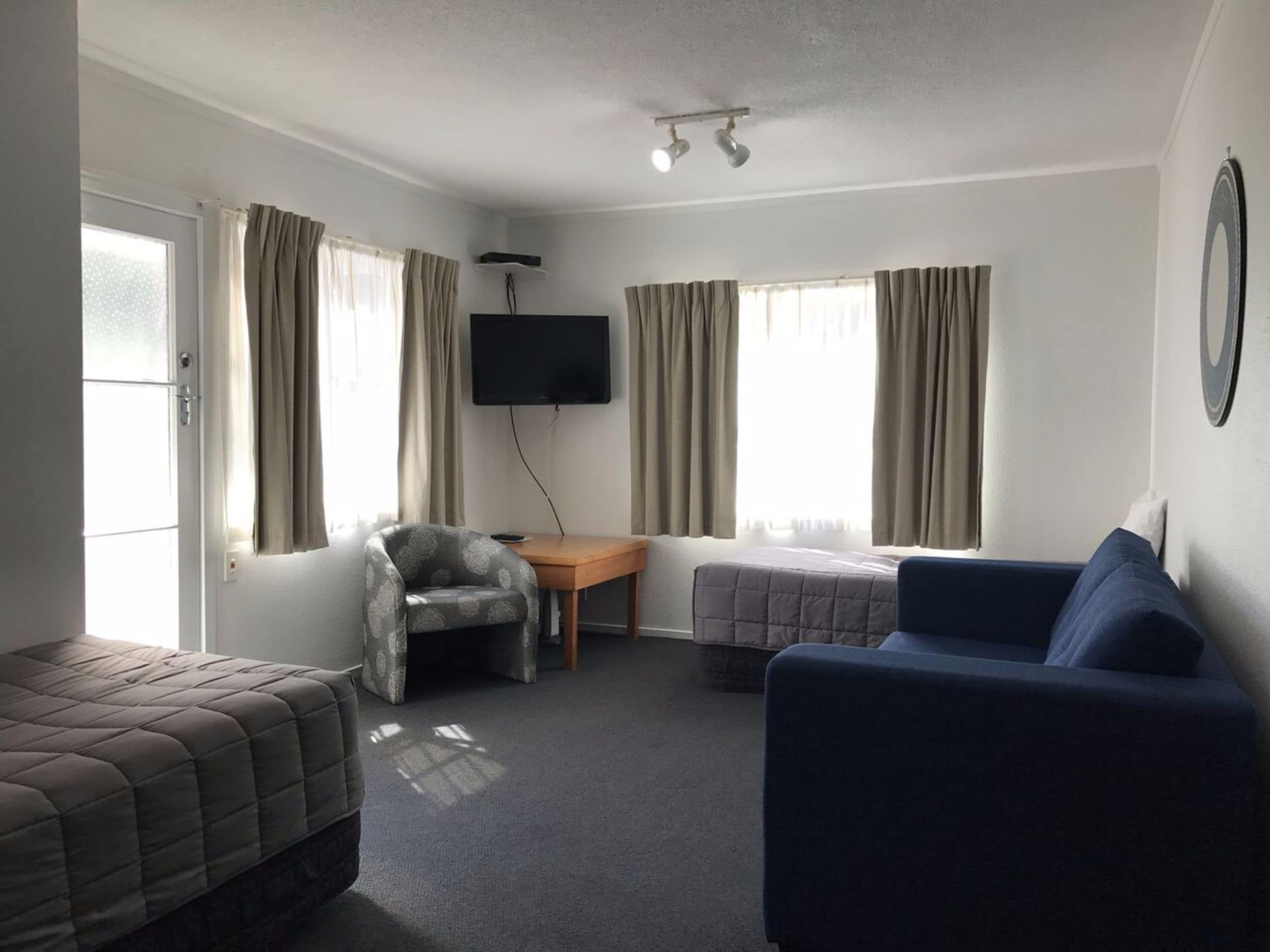 A room with a bed, a blue sofa, a chair, a TV, and a small table.