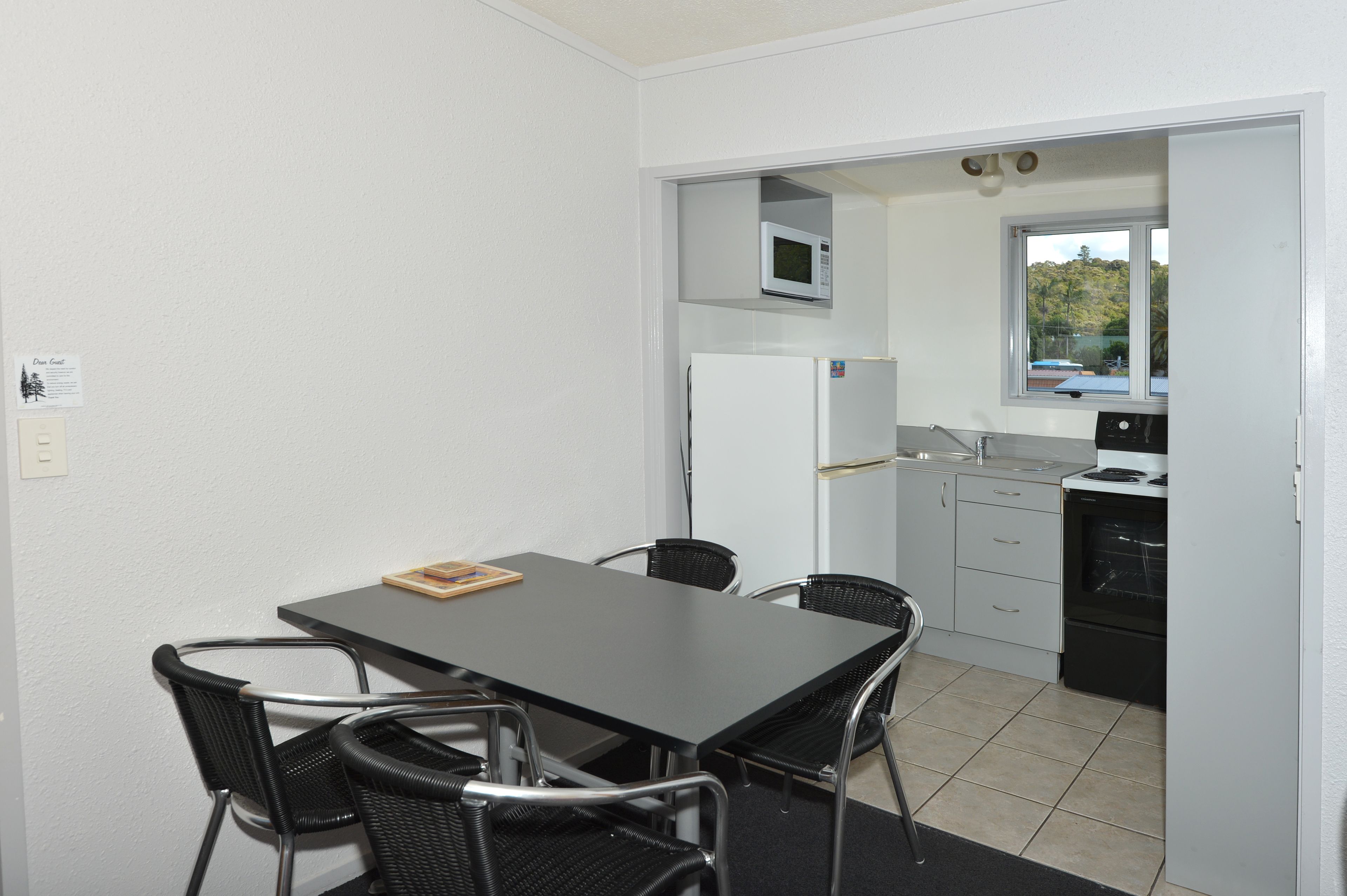 Una cocina compacta con microondas, refrigerador y horno. Hay una mesa de comedor con sillas y un ventanal con vistas al exterior.