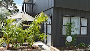A modern building with a dark exterior, large windows, and a well-maintained garden with palm trees and a patio umbrella. - Edelweiss Motel (Paihia)