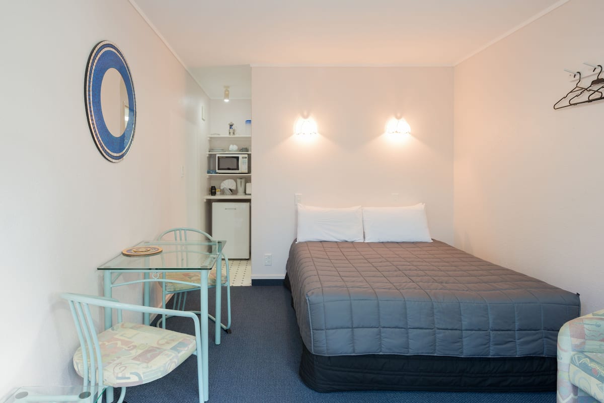 A small, compact room with a single bed, a table with a chair, and a microwave.
